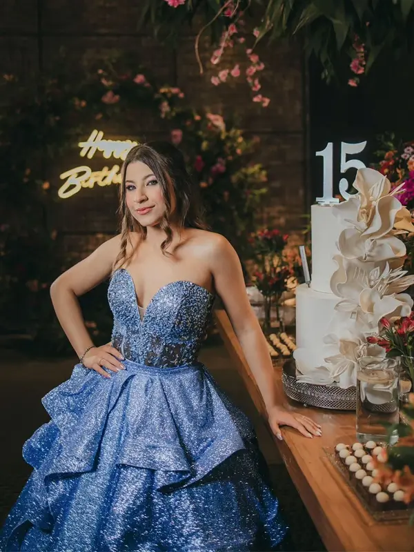 Debutante de vestido azul ao lado do bolo